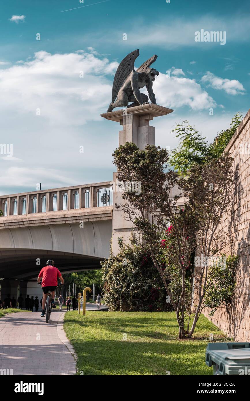 Homme faisant du vélo sous un pont dans la Cité des Arts et des Sciences, où un gargouille se profile au-dessus de lui, Valence, Espagne Banque D'Images