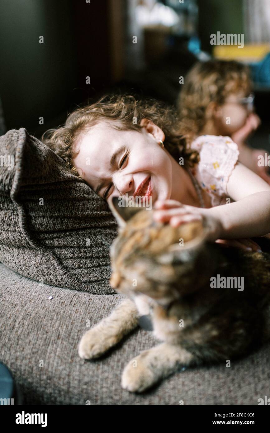 Petite fille jouant avec son chat sur le canapé dedans le salon Banque D'Images