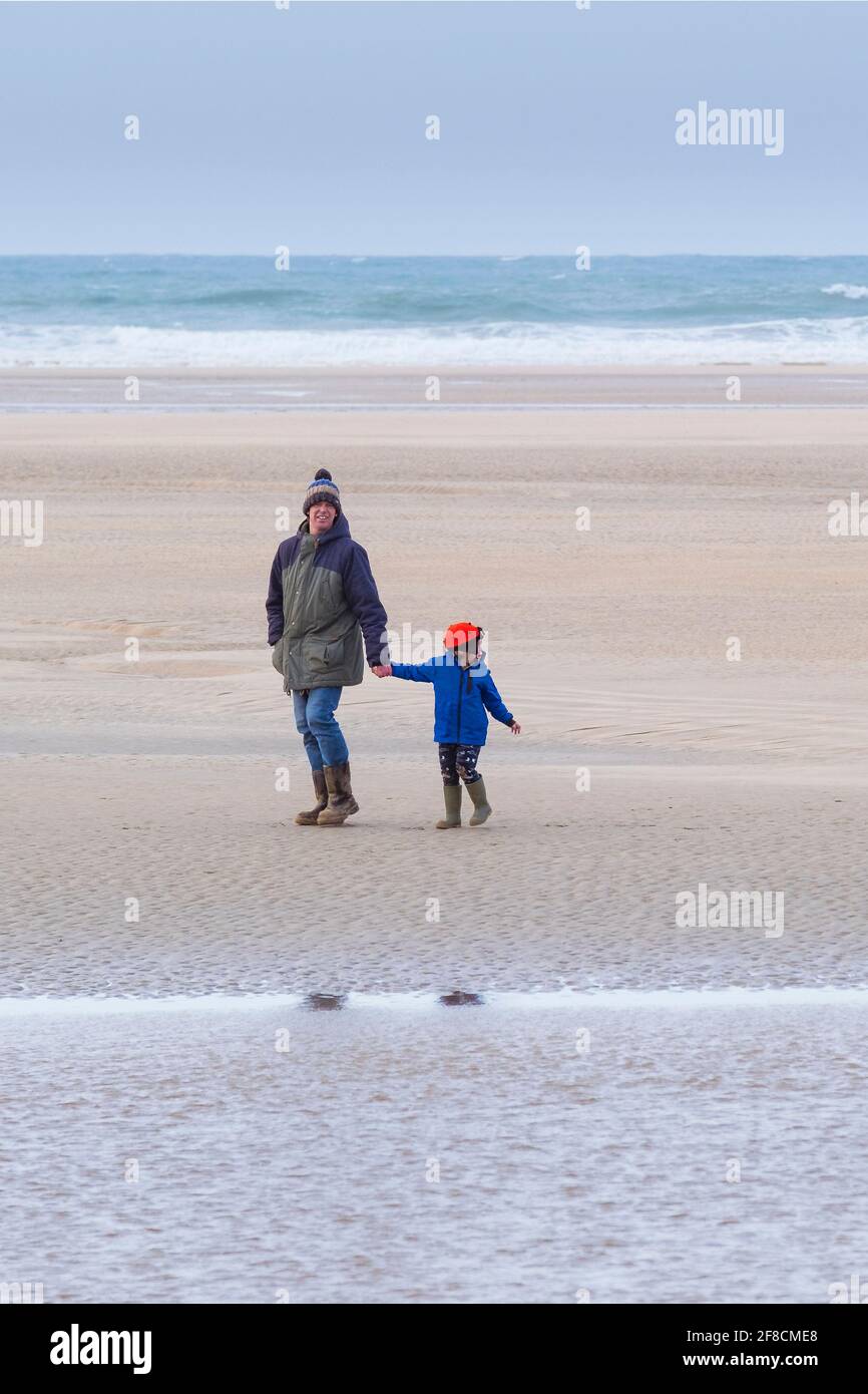 Un père et un enfant qui profite d'une promenade sur une plage froide de Crantock à Newquay, dans les Cornouailles. Banque D'Images