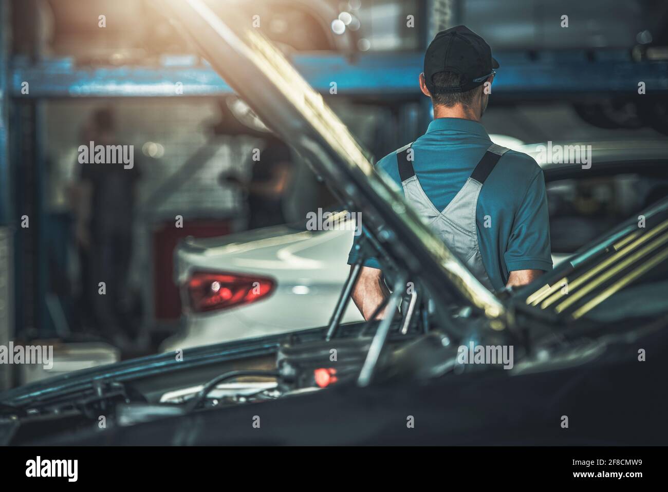 Employé du centre de service automobile restant entre les véhicules à l'intérieur du bâtiment d'entretien automobile. Thème de l'industrie du transport. Les hommes de race blanche dans ses années 30. Banque D'Images