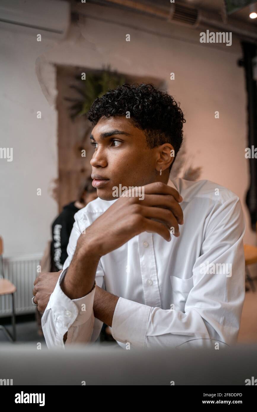 Un jeune homme noir est assis à la table avec un ordinateur portable, buvant du thé et utilisant un smartphone. Le gars dans le café. Travailler à distance en dehors du bureau Banque D'Images