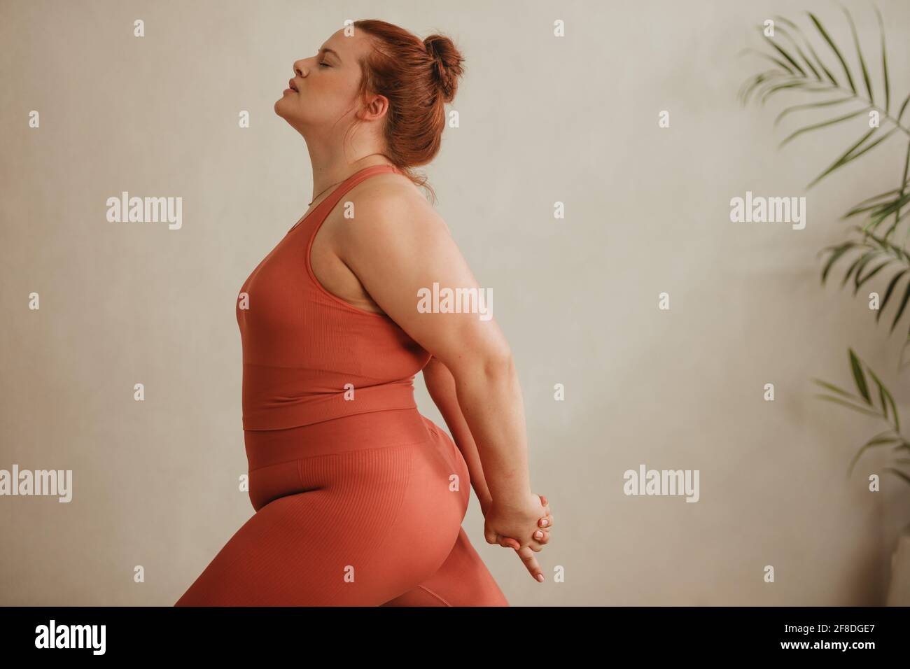 Vue latérale d'une femme forte qui fait de l'exercice. Plus grande taille femme en vêtements de sport faisant quelques exercices d'étirement avec la main clased derrière. Banque D'Images