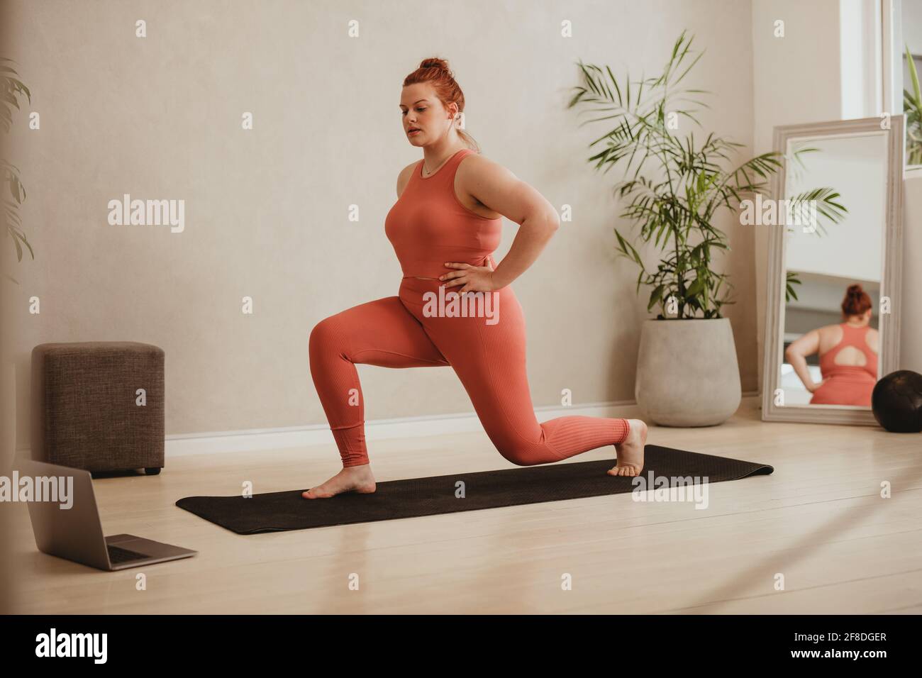 Plus de taille femme dans les vêtements de sport faire l'entraînement de fente regardant l'entraînement en ligne. Femme s'entraînant sur un cours d'entraînement en ligne sur son ordinateur portable. Banque D'Images
