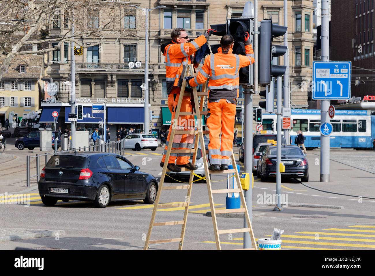 Zurich Bellevue, Suisse - 10 mars 2021 : deux ouvriers d'entretien en orange avertissent les vêtements de réparer un signal de circulation, par jour Banque D'Images
