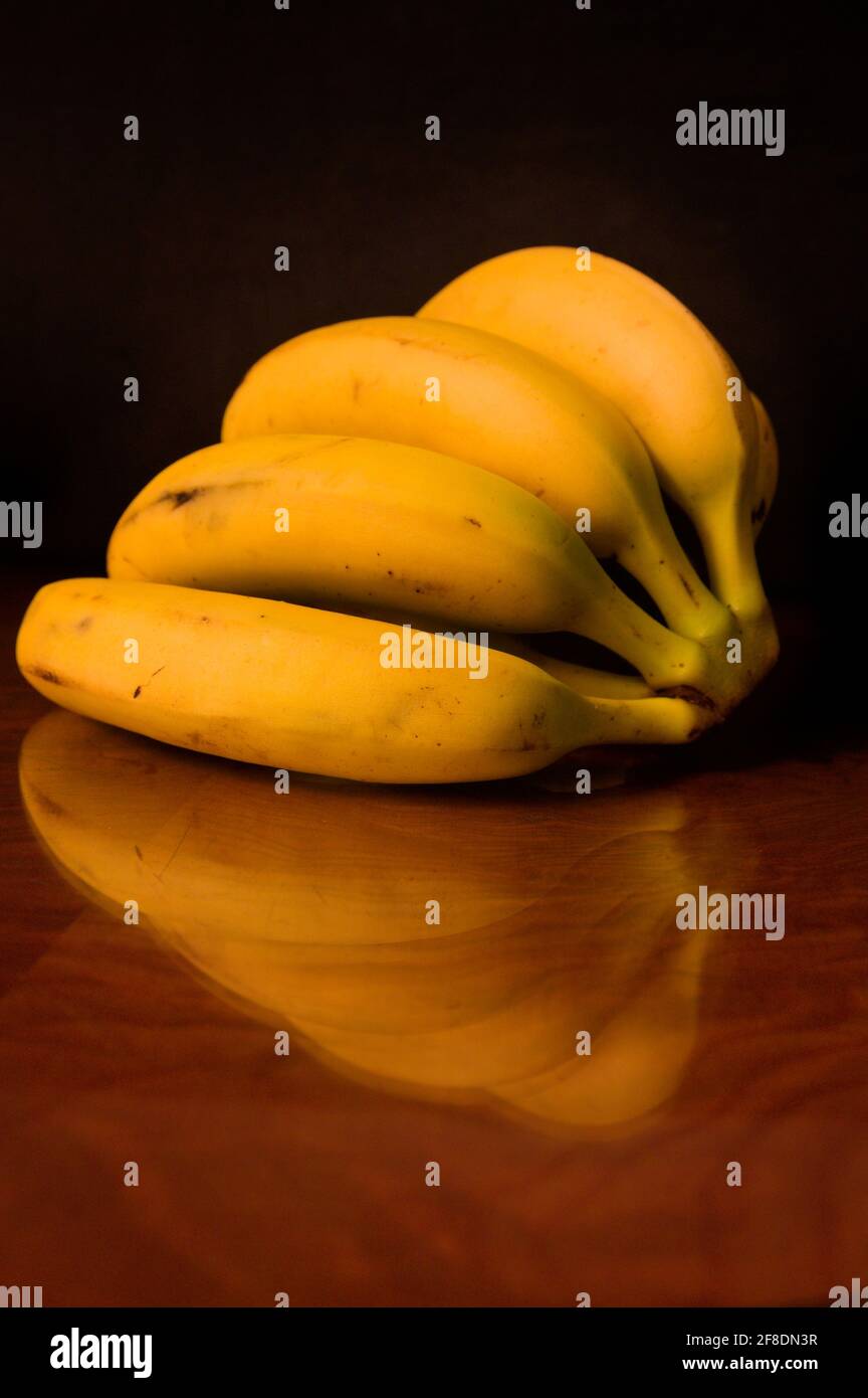 Une main de bananes sur une table en bois sombre dans laquelle elle se reflète, avec un fond sombre Banque D'Images