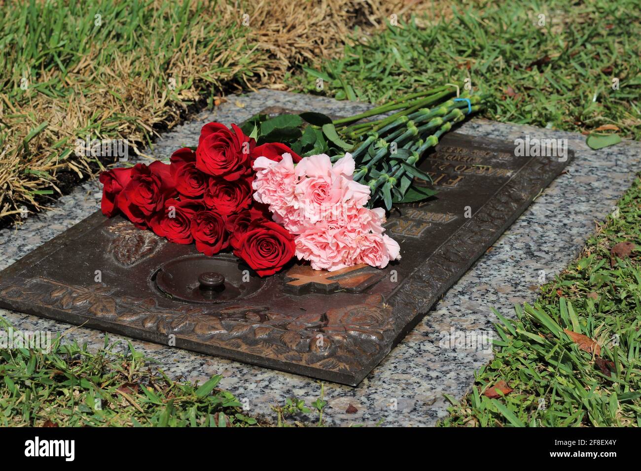 Des roses rouges et des fleurs de la carnation qui se trouvent sur une plaque de cimetière d'un bien-aimé perdu. Cimetière, perte d'un concept aimé un. Banque D'Images