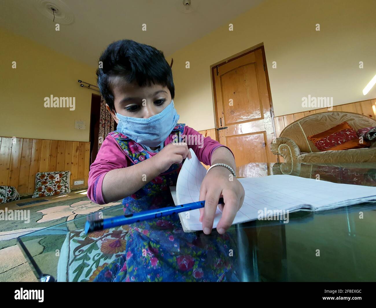 Des élèves masqués lisant et écrivant leur travail scolaire à la maison pendant le coronavirus pandémique. Les cours en ligne sont courants en raison de Covid 19. Banque D'Images