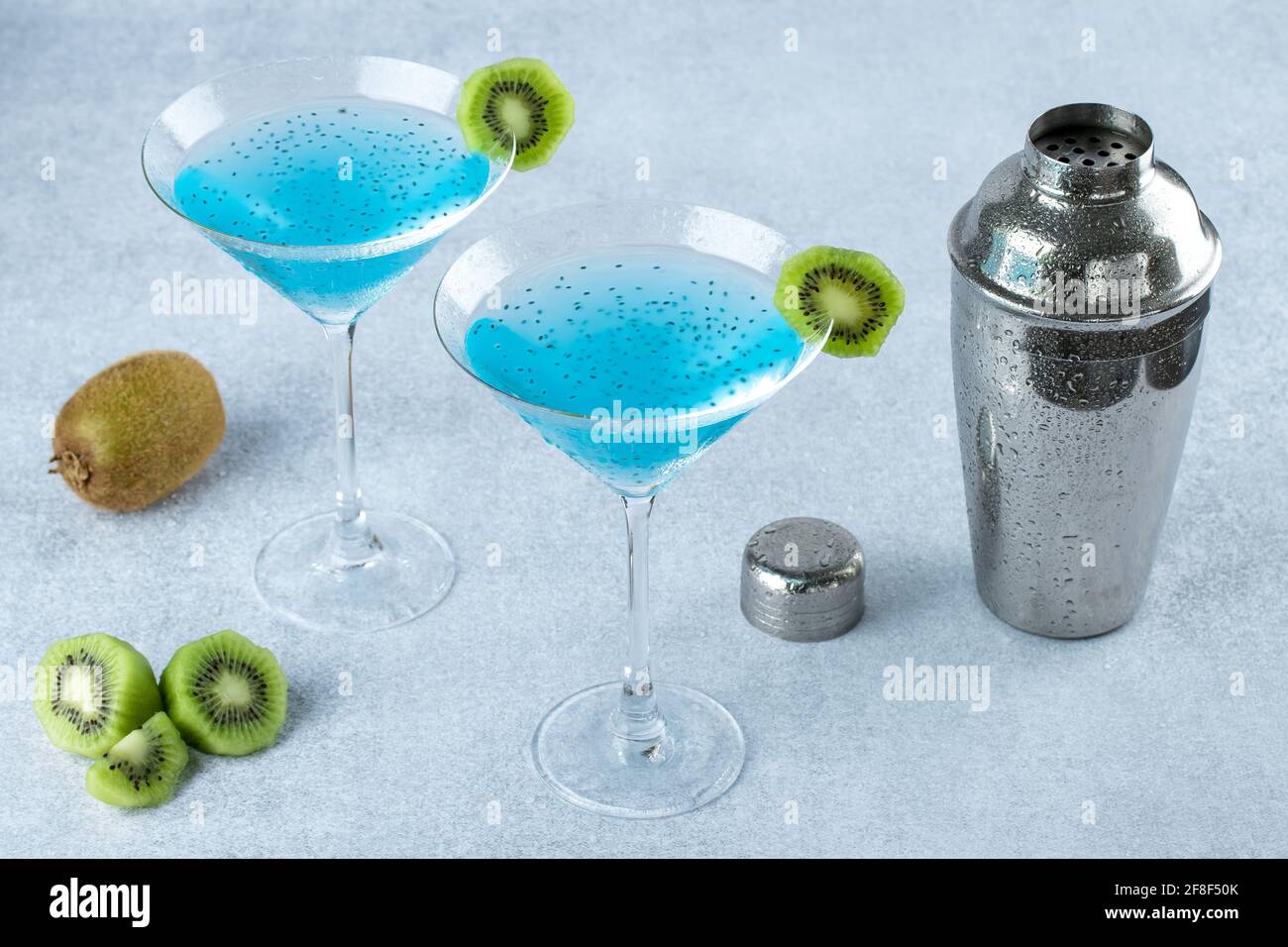 Deux verres de martini avec kiwi et shaker à cocktail en métal sur fond gris. curaçao bleu avec graines et agitateur à cobbler refroidi, boisson alcoolisée, réf Banque D'Images