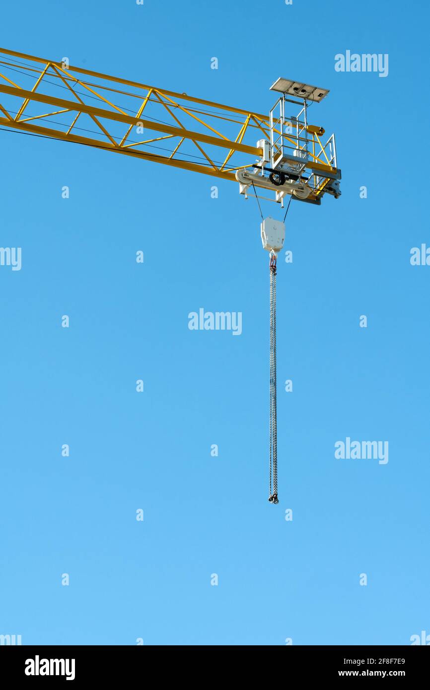 Une grue de construction jaune faite de tuyaux en acier avec un crochet sur lequel porte une chaîne contre un ciel bleu. Banque D'Images