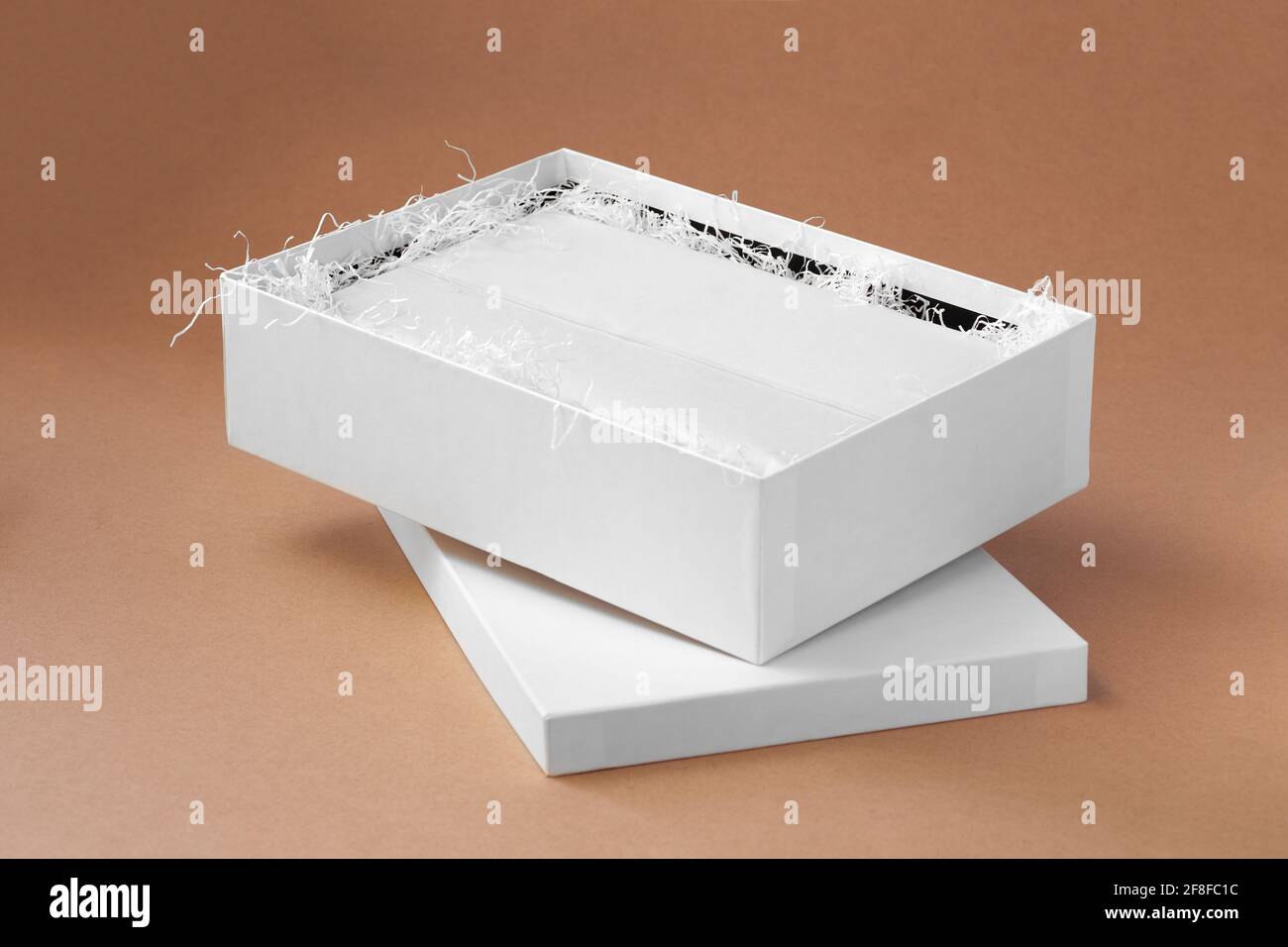 faites une maquette d'une boîte ouverte blanche avec des vêtements dans un propre papier de soie blanc vierge et papier déchiqueté pour la protection sur arrière-plan en papier beige Banque D'Images