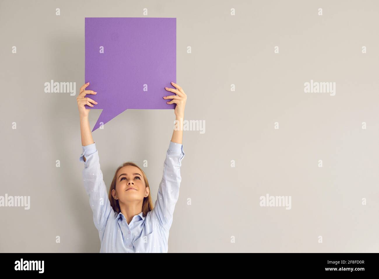 Une jeune femme heureuse tenant debout une bulle de parole violette vide sur fond gris Banque D'Images