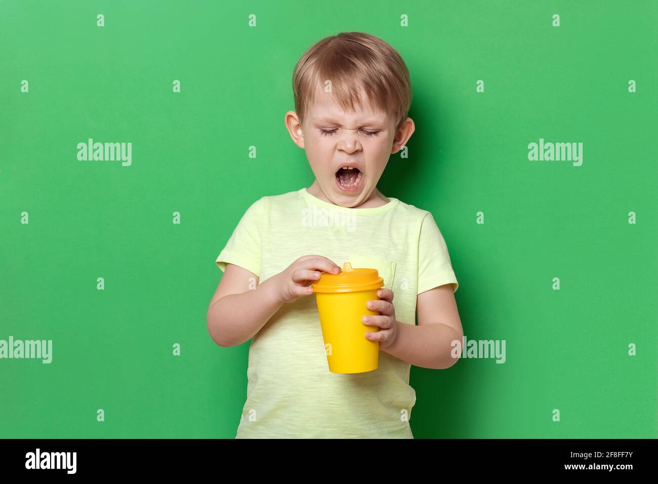 Personnes enfant garçon garçon bât café ouvert jaune papier jetable tasse. Concept de lundi matin dur, envie de dormir, fatigue. Studio tourné au dos vert Banque D'Images
