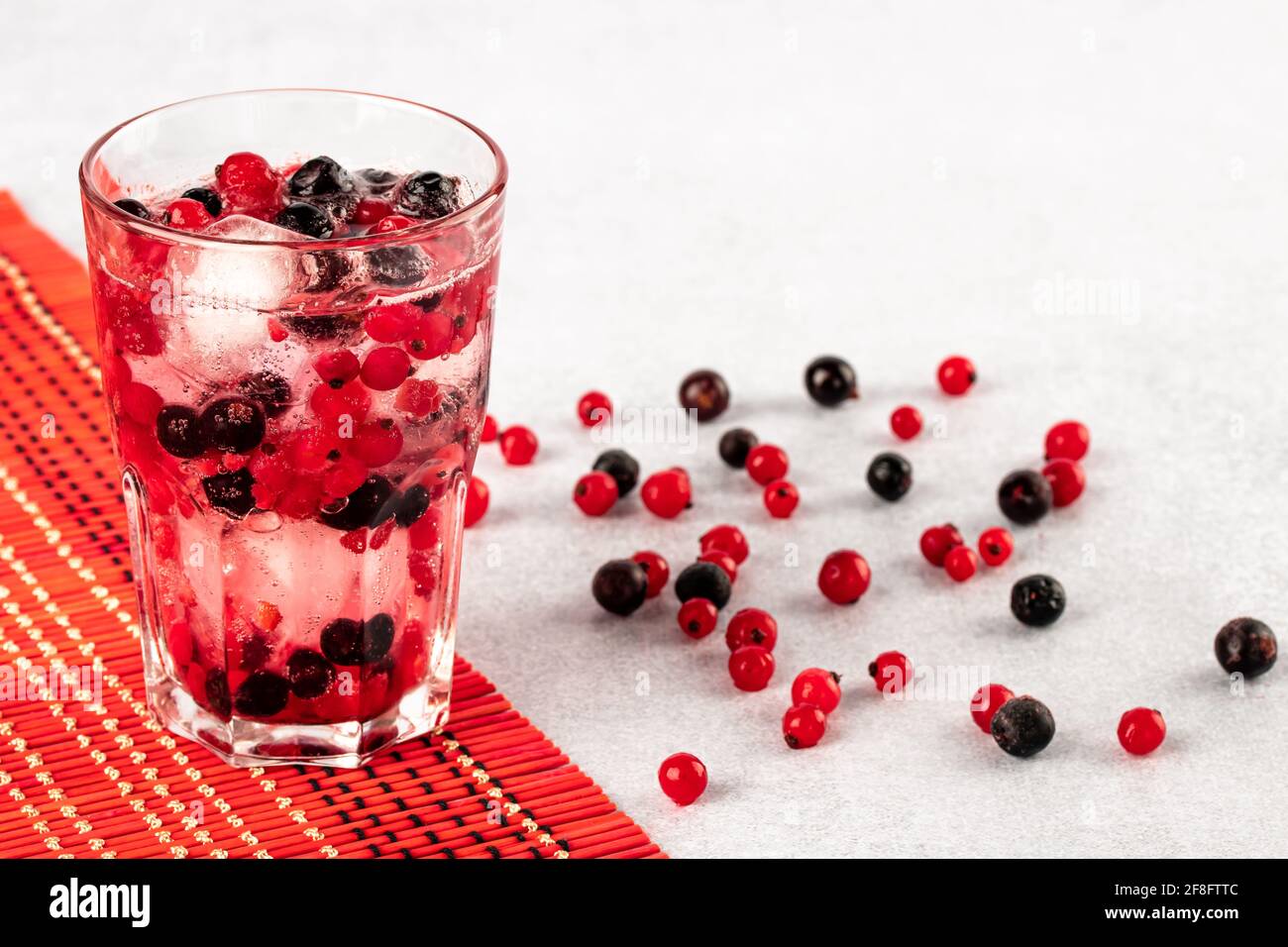 Boisson fraîche d'été avec eau, glace et baies multicolores. Un verre de raisins de Corinthe rouges et noirs sur fond gris. Fruitarianisme, concept de veganisme. Vég Banque D'Images