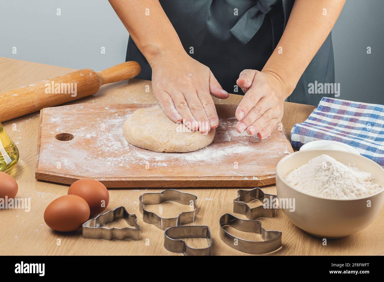 Les mains des femmes dans la farine pétrir la pâte pour des biscuits sablés faits maison sur un panneau de bois. À proximité sont un rollpin, des oeufs, des emporte-pièces métalliques, de la farine, Banque D'Images