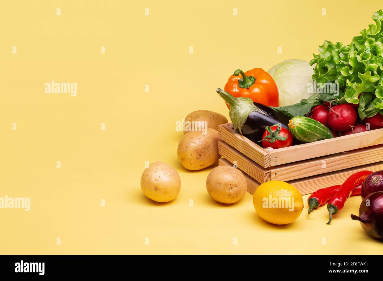 Pommes de terre de légumes frais, aubergines, chou, radis, concombres, citron, laitue, poivre, tomate, dans une boîte en bois sur fond jaune clair. Banque D'Images
