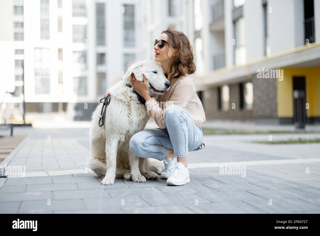 Une femme joyeuse joue et se hale avec son grand chien blanc heureux dans la rue. Animaux acceptés et concept de soins pour animaux. Amoureux des animaux. Banque D'Images