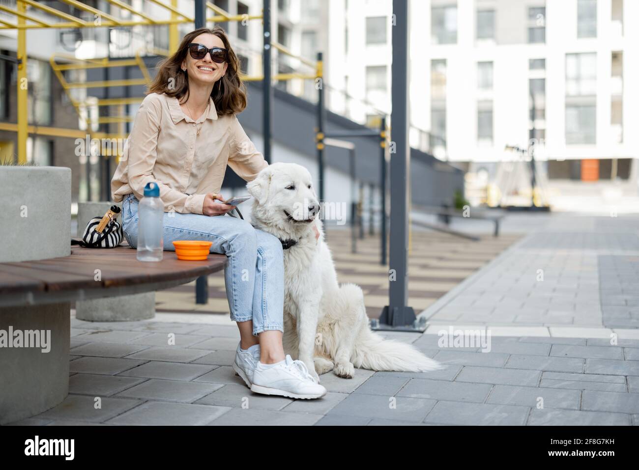 Femme gaie assise sur le banc avec un grand chien blanc dans la cour de la résidence. Amoureux des animaux, propriétaire acceptant les animaux. Banque D'Images