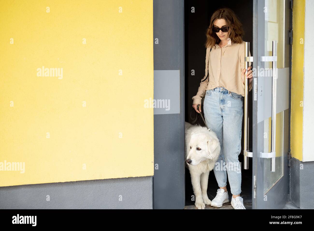 Jolie femme ouvre la porte d'entrée du bâtiment et va pour une promenade avec le chien dans la cour de la résidence. Amoureux des animaux, propriétaire acceptant les animaux. Banque D'Images