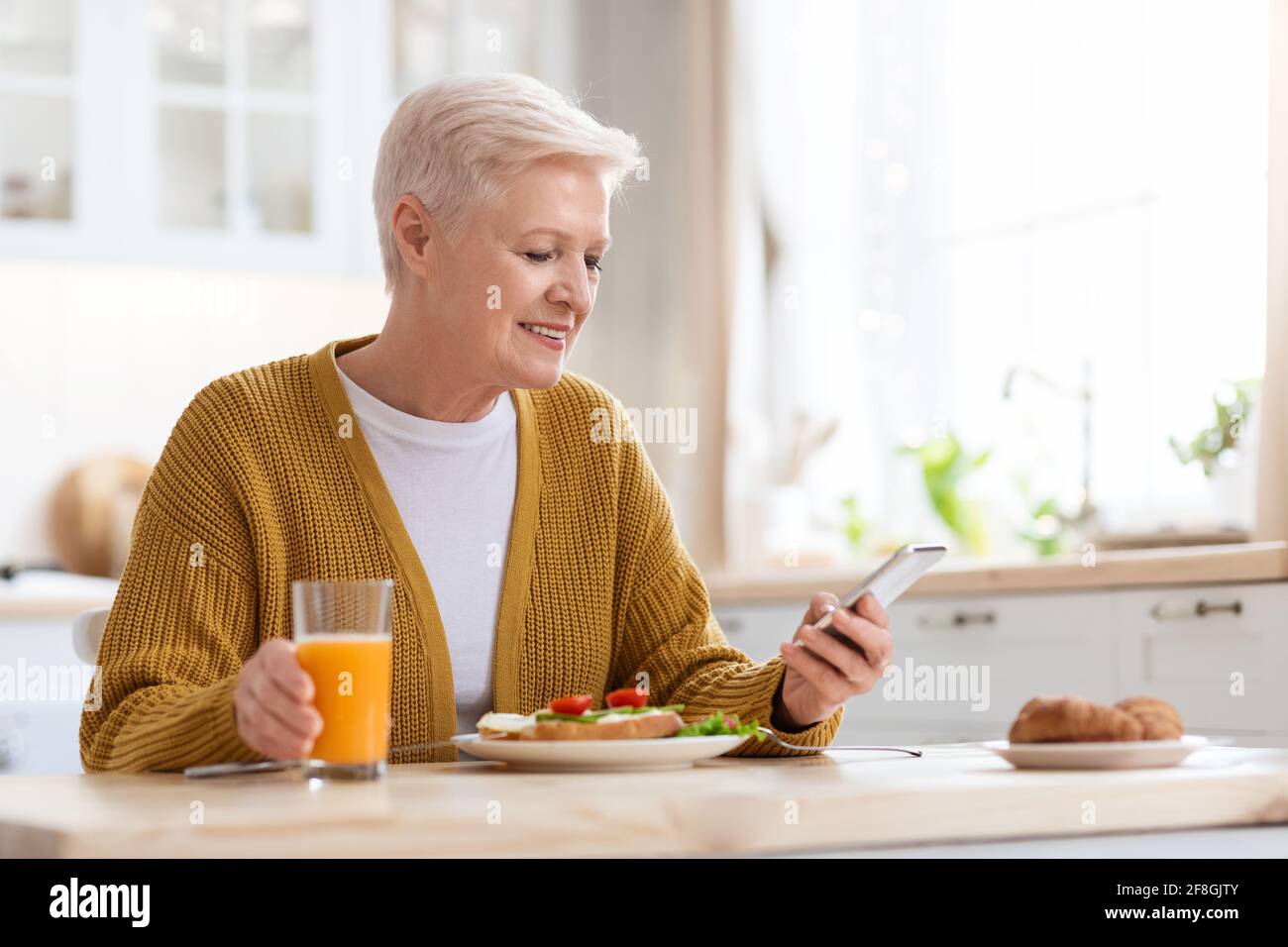 Femme sénior ayant déjeuné et utilisant un smartphone Banque D'Images