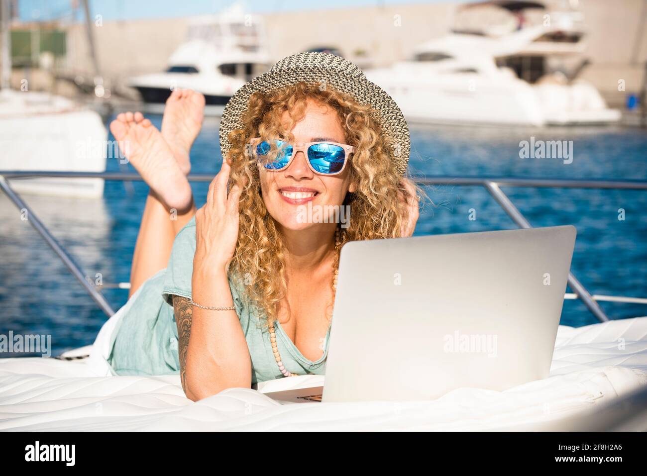 Jeune femme assez adulte sourire et utiliser un ordinateur portable à l'extérieur couchez-vous sur le pont d'un yacht - voyage et vacances d'été style de vie et mod Banque D'Images