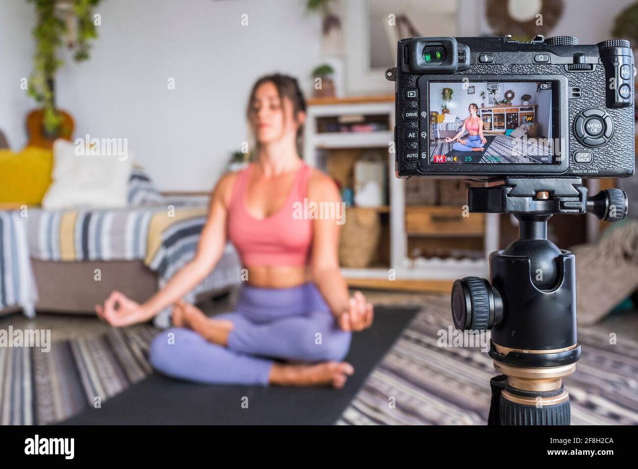 Jeune femme s'exerçant à la maison faisant pilates et l'enregistrement à elle dispose d'un appareil photo numérique pour enseigner l'entraînement et produire du web classe - les affaires du créateur de contenu Banque D'Images