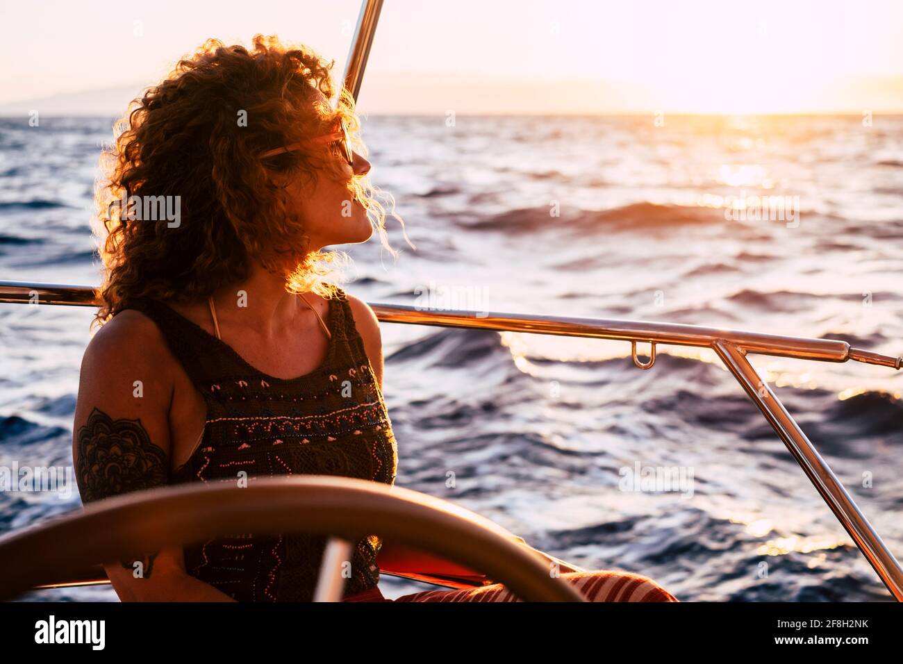 Gaie et attrayante jeune femme blonde adulte sourire et profiter de la excursion assise sur le pont en voilier qui regarde le bleu mer autour - concept de Banque D'Images