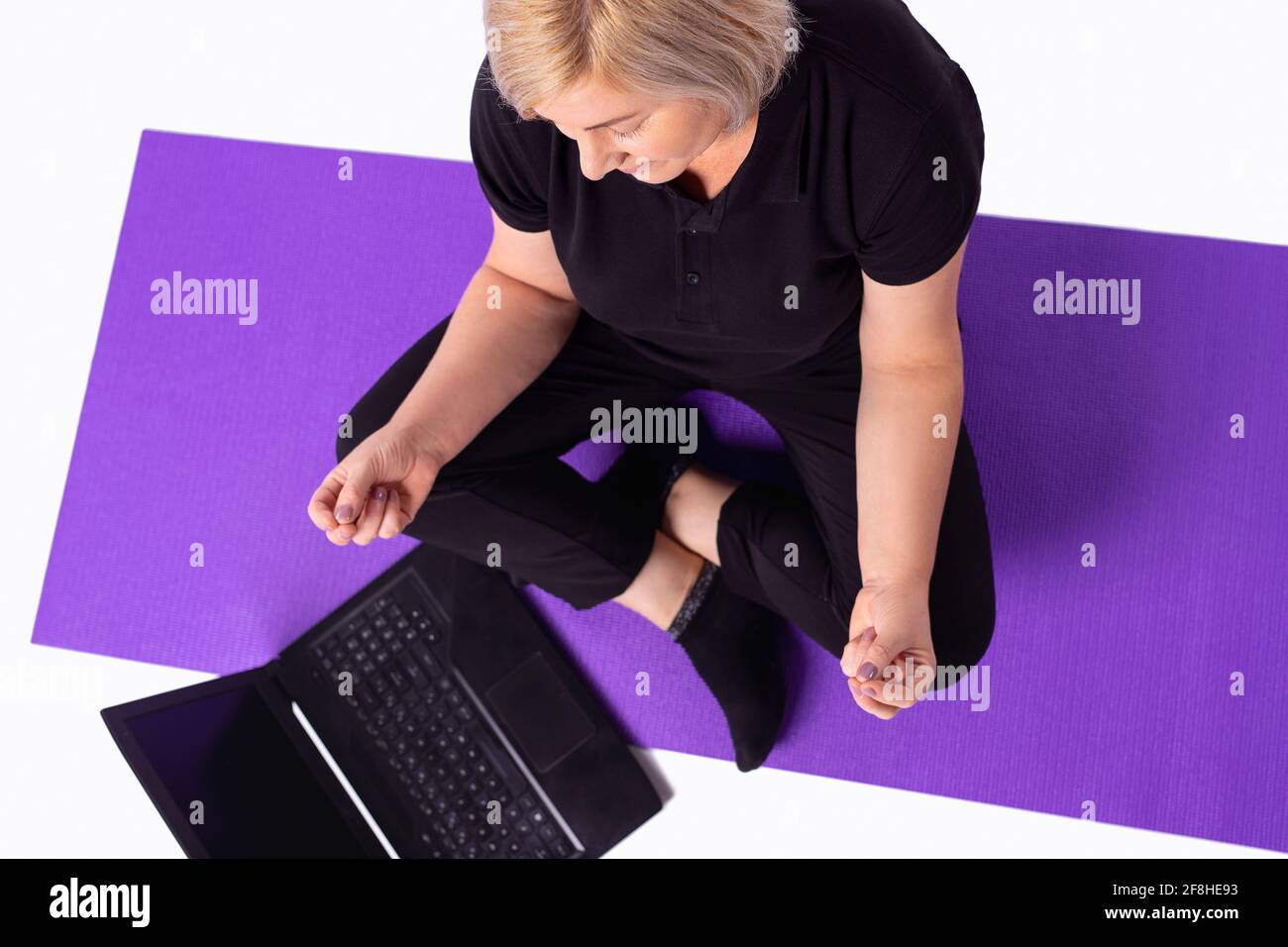 Senior en bonne santé calme femme blonde cheveux dans sportswear méditer regarder en ligne cours sur ordinateur portable à la maison. Mettre en forme les personnes âgées sportives en train de faire du yoga Banque D'Images