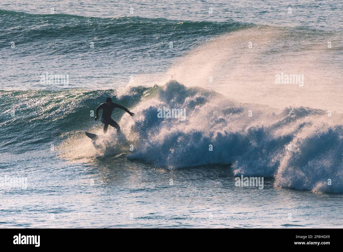 Un surfeur qui fait une vague et silhoueté par la lumière du début de soirée à Fistral à Newquay en Cornouailles. Banque D'Images