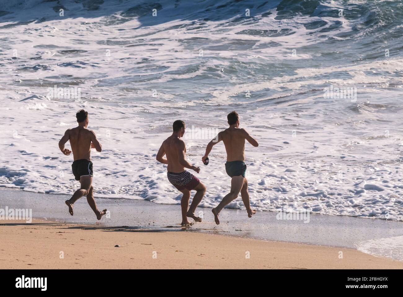 Des vacanciers mâles qui se rendient dans la mer à Fistral Beach à Newquay, en Cornouailles. Banque D'Images