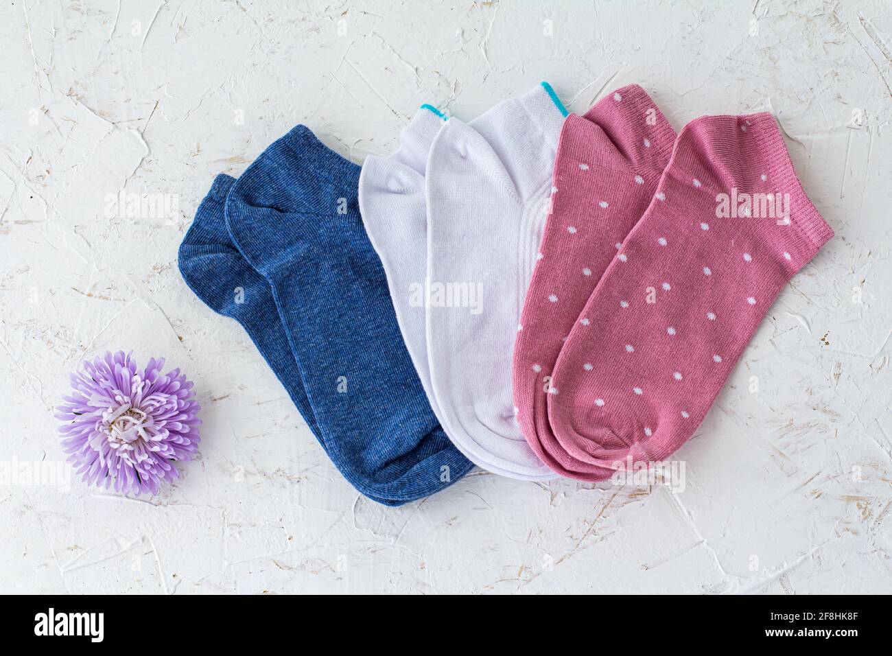 Trois paires de chaussettes bleues, blanches et roses pour femmes avec une fleur d'aster sur fond blanc structuré, vue du dessus. Banque D'Images