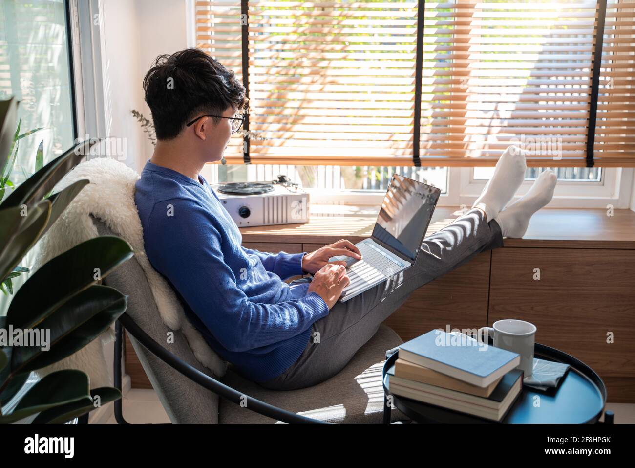 Jeune homme asiatique de technologie se détendant tenant un ordinateur portable et regardant l'écran dans le salon, travail à distance ou le concept de travail à domicile Banque D'Images