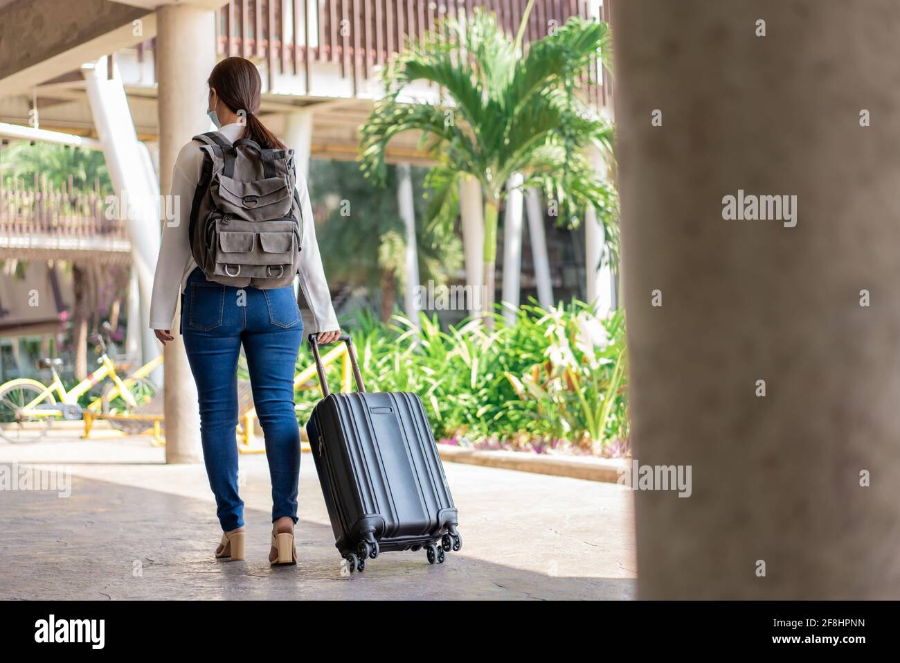 Déplacement. Une femme dans une chemise blanche à manches longues et un  Jean, portant un masque. Retournez et marchez avec la valise dans la main  droite et le sac à dos Photo