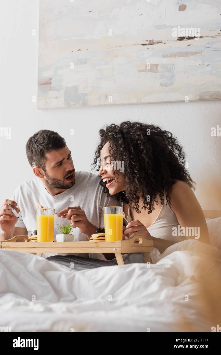 homme barbu choqué regardant la bonne amie afro-américaine avoir petit déjeuner Banque D'Images