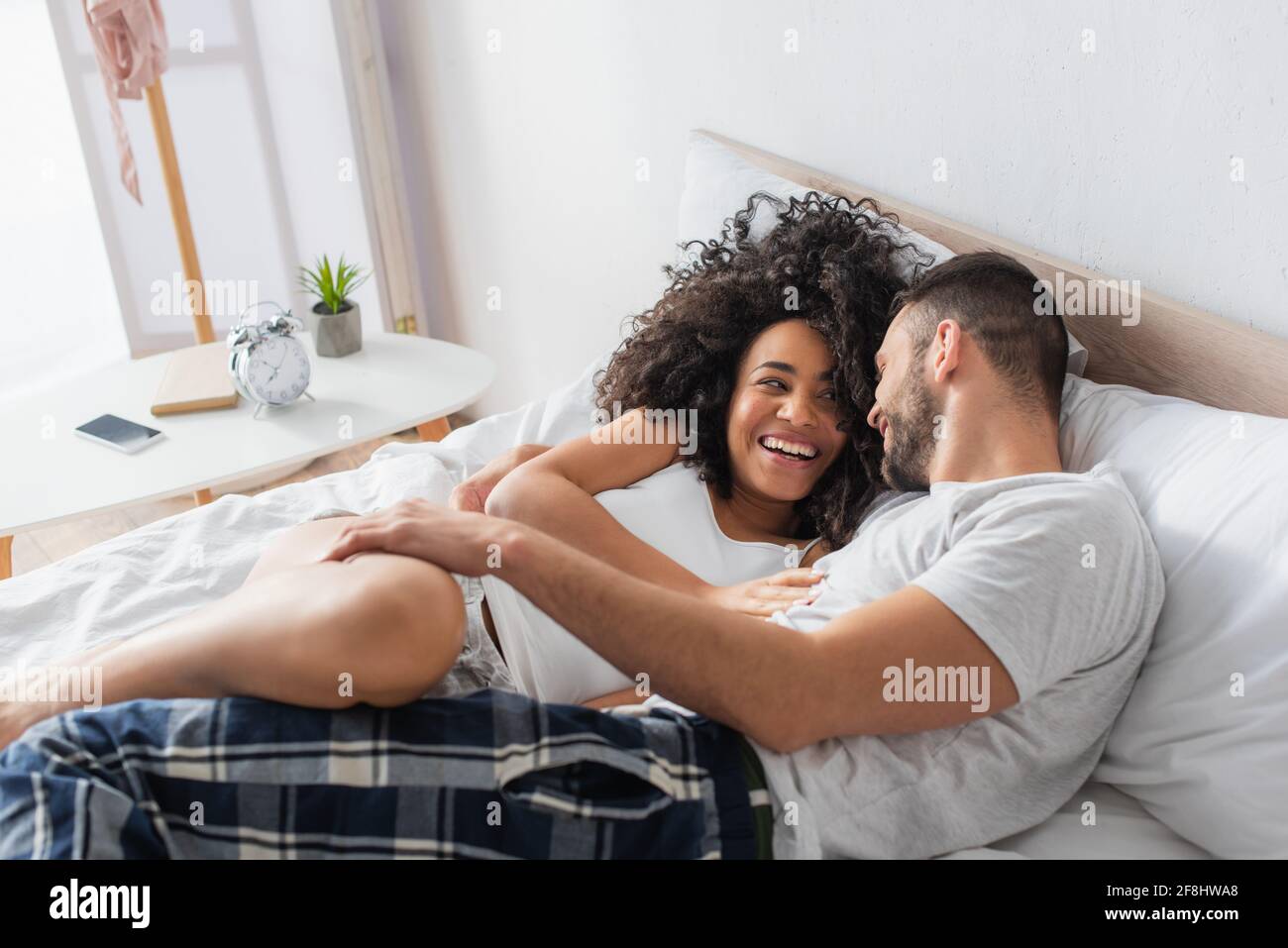 couple interracial gai souriant et allongé sur le lit Banque D'Images