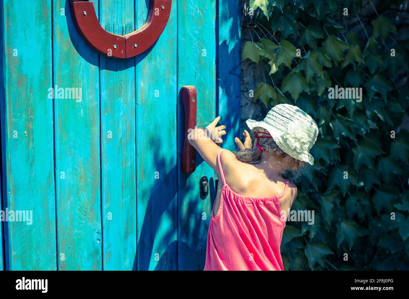 curieuse petite fille essayant d'ouvrir une porte en bois verrouillée Banque D'Images