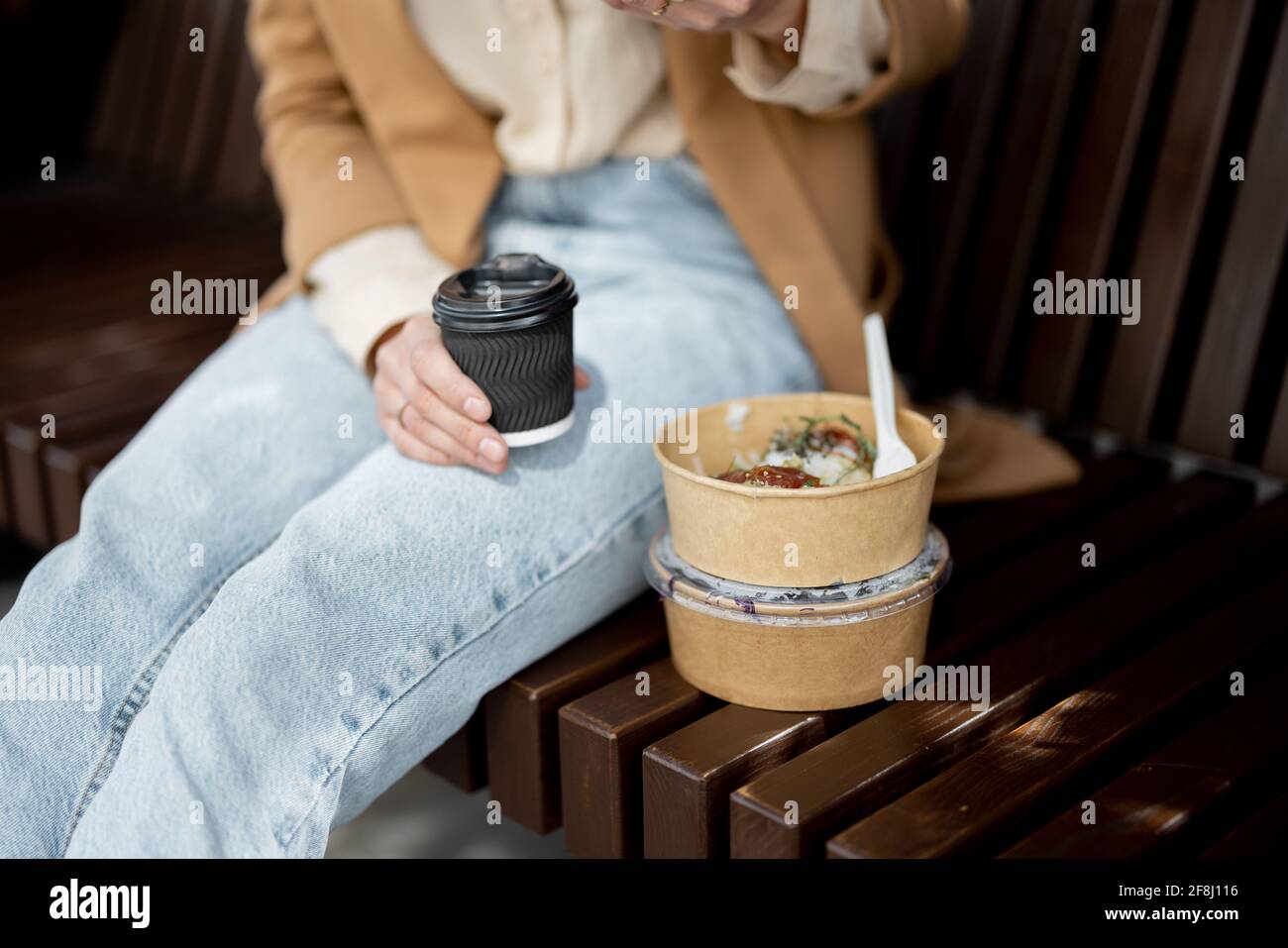 Jolie femme ont un déjeuner extérieur près du bâtiment de bureau tout en étant assise sur la banquette. Repas sain et café à emporter pour les travailleurs. Gros plan Banque D'Images