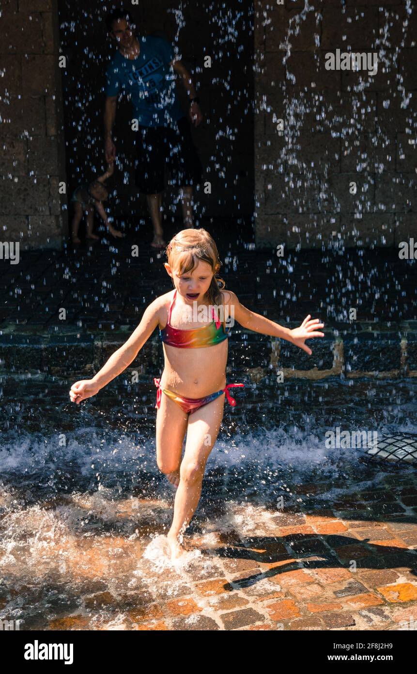petite fille blonde jouant avec de l'eau et courant dans l'eau gouttes Banque D'Images