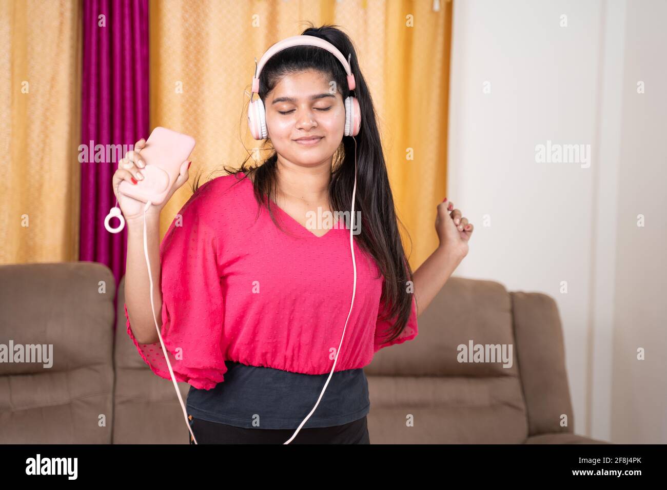 Photo moyenne d'une jeune fille dansant en écoutant de la musique à partir d'écouteurs connectés au mobile après l'entraînement dans le salon - concept de détente, joyeuse Banque D'Images