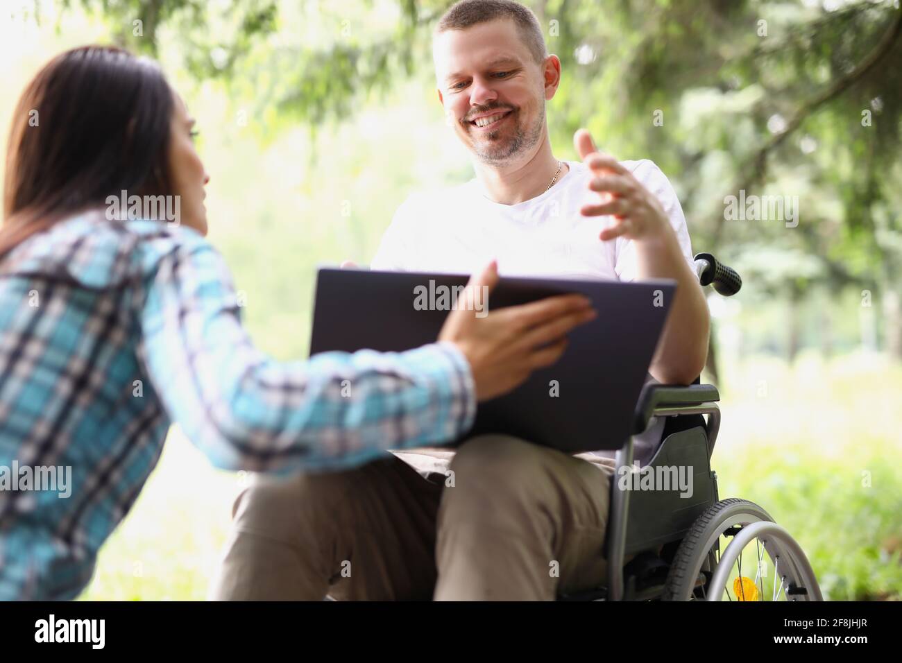 Jeune homme en fauteuil roulant et femme regardant l'écran d'ordinateur portable dans le parc Banque D'Images