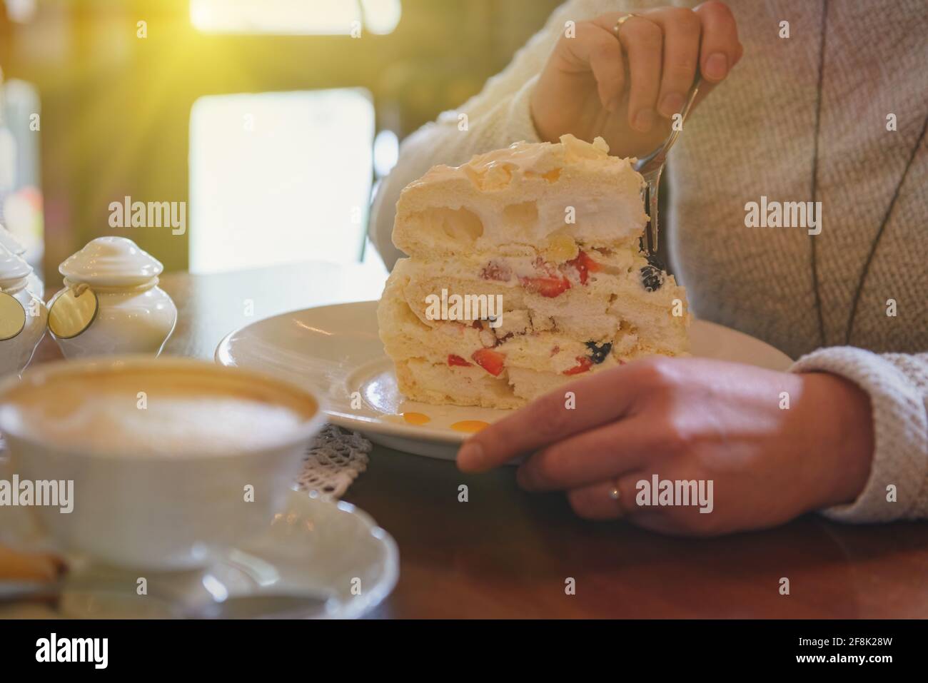 Image authentique d'une femme mangeant un gâteau meringue, une tasse de cappuccino en arrière-plan Banque D'Images