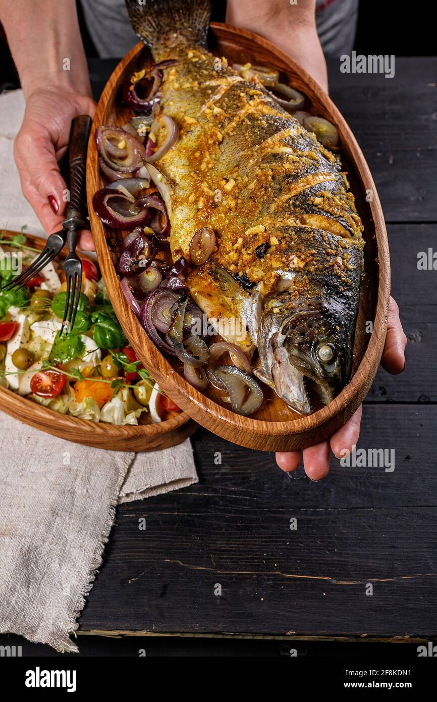 Salade de fruits de mer et de légumes. Un déjeuner délicieux et sain. Les mains des femmes tiennent un plat en bois avec du poisson grillé. Régime méditerranéen. Tir vertical. Nourriture p Banque D'Images