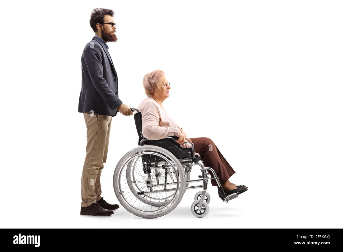 Prise de vue sur toute la longueur d'un homme barbu poussant un femme âgée assise dans un fauteuil roulant isolé sur fond blanc Banque D'Images