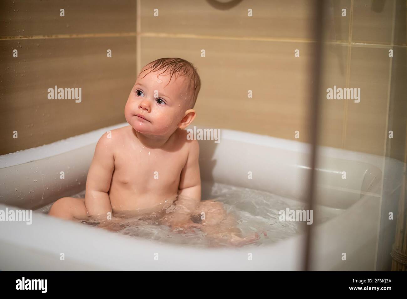 Petite fille charmante babe joue dans l'eau dans la petite piscine  gonflable de bébé située dans la cabine de douche dans la salle de bains,  fille de bébé souriant et d'avoir le