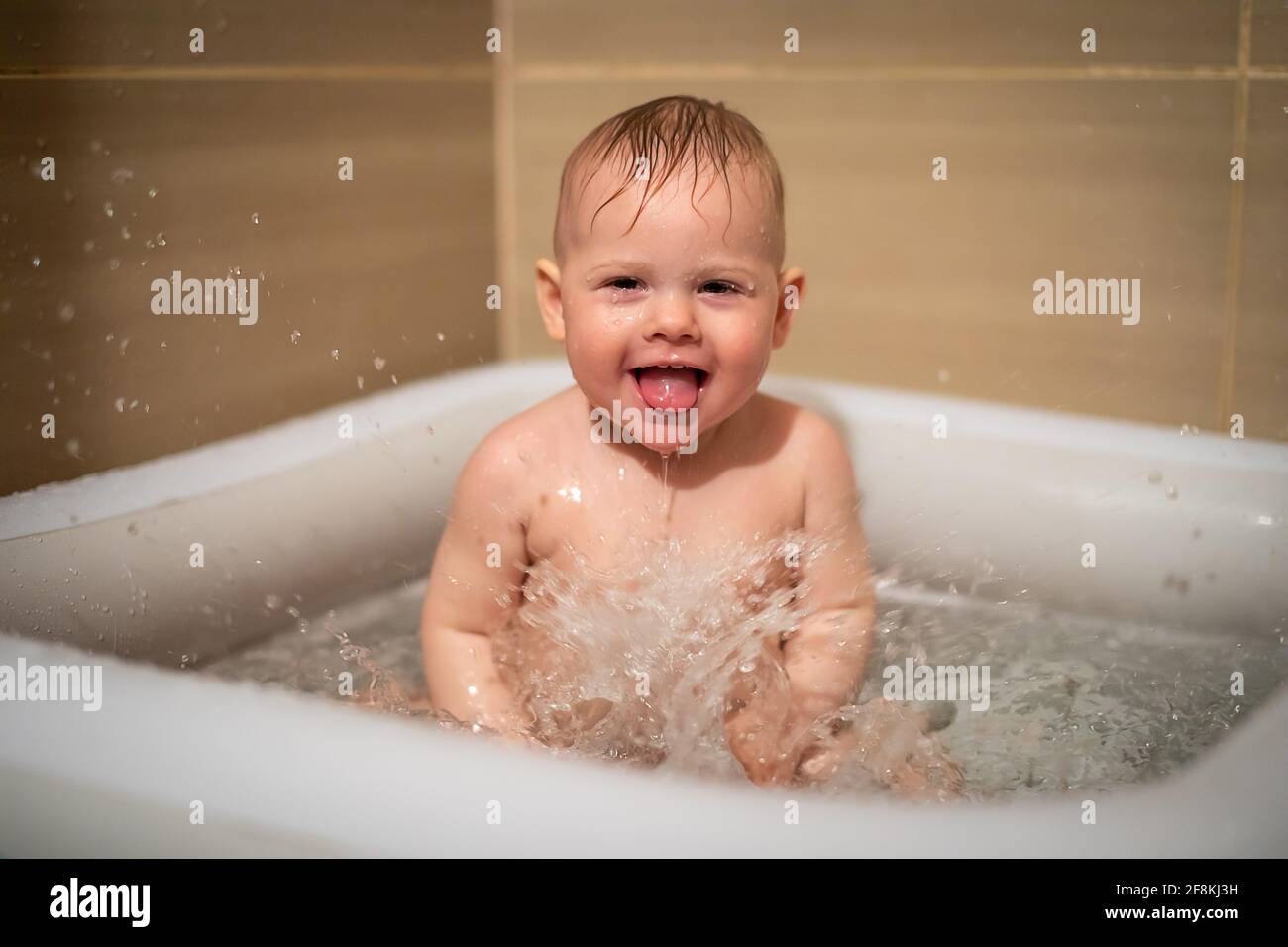 Petite fille charmante babe joue dans l'eau dans la petite piscine  gonflable de bébé située dans la cabine de douche dans la salle de bains,  fille de bébé souriant et d'avoir le