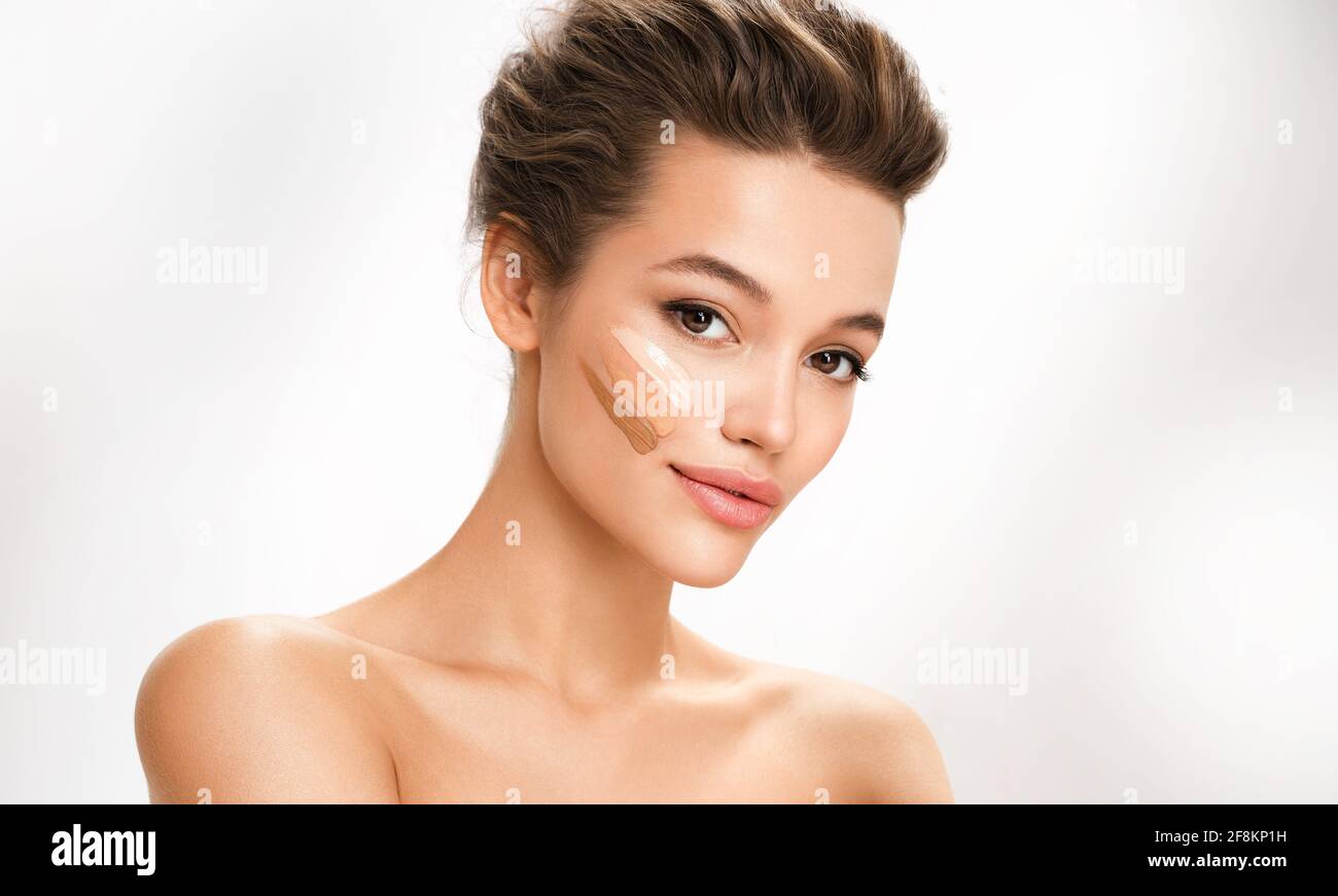 Belle femme avec des lignes de crème ton sur son visage. Photo d'une femme brune avec maquillage parfait sur fond blanc. Concept de soins de la peau Banque D'Images