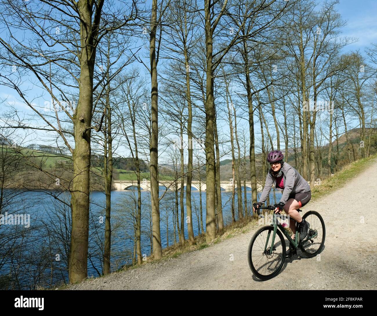 Les cyclistes apprécient le soleil printanier en longeant le réservoir Ladybower, dans le nord du Derbyshire, avec le viaduc d'Ashopton en arrière-plan. Banque D'Images