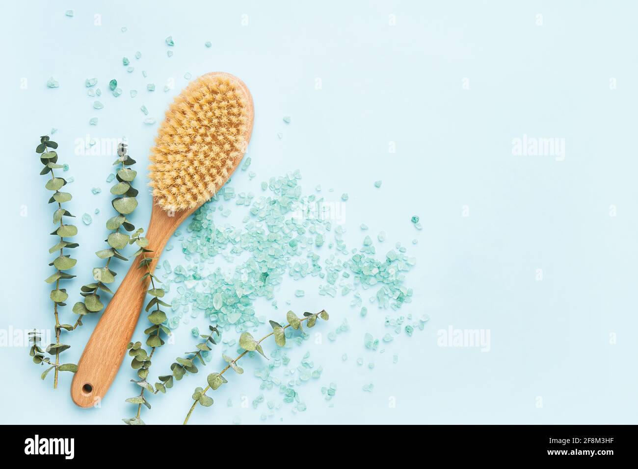 Concept DE soins SPA. Brosse anti-cellulite pour le corps, branches d'eucalyptus et sel de bain sur fond bleu. Vue de dessus, espace de copie pour le texte Banque D'Images