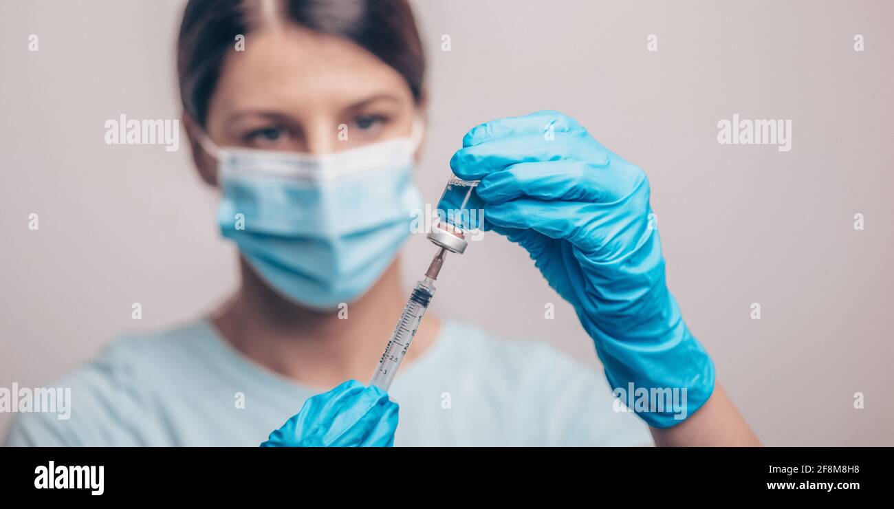 Médecin dans des gants et un masque de protection contenant un flacon en verre avec du liquide injectable. Vaccin contre la grippe et le coronavirus. Photo Banque D'Images