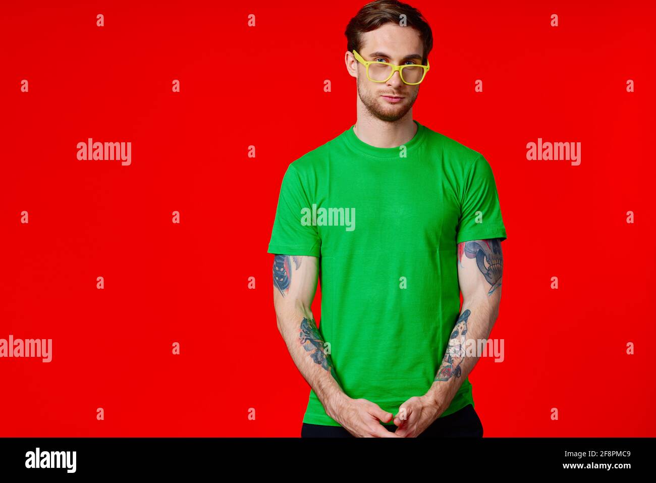 un homme dans un t-shirt vert avec des tatouages dans son mains portant des lunettes sur fond rouge Banque D'Images