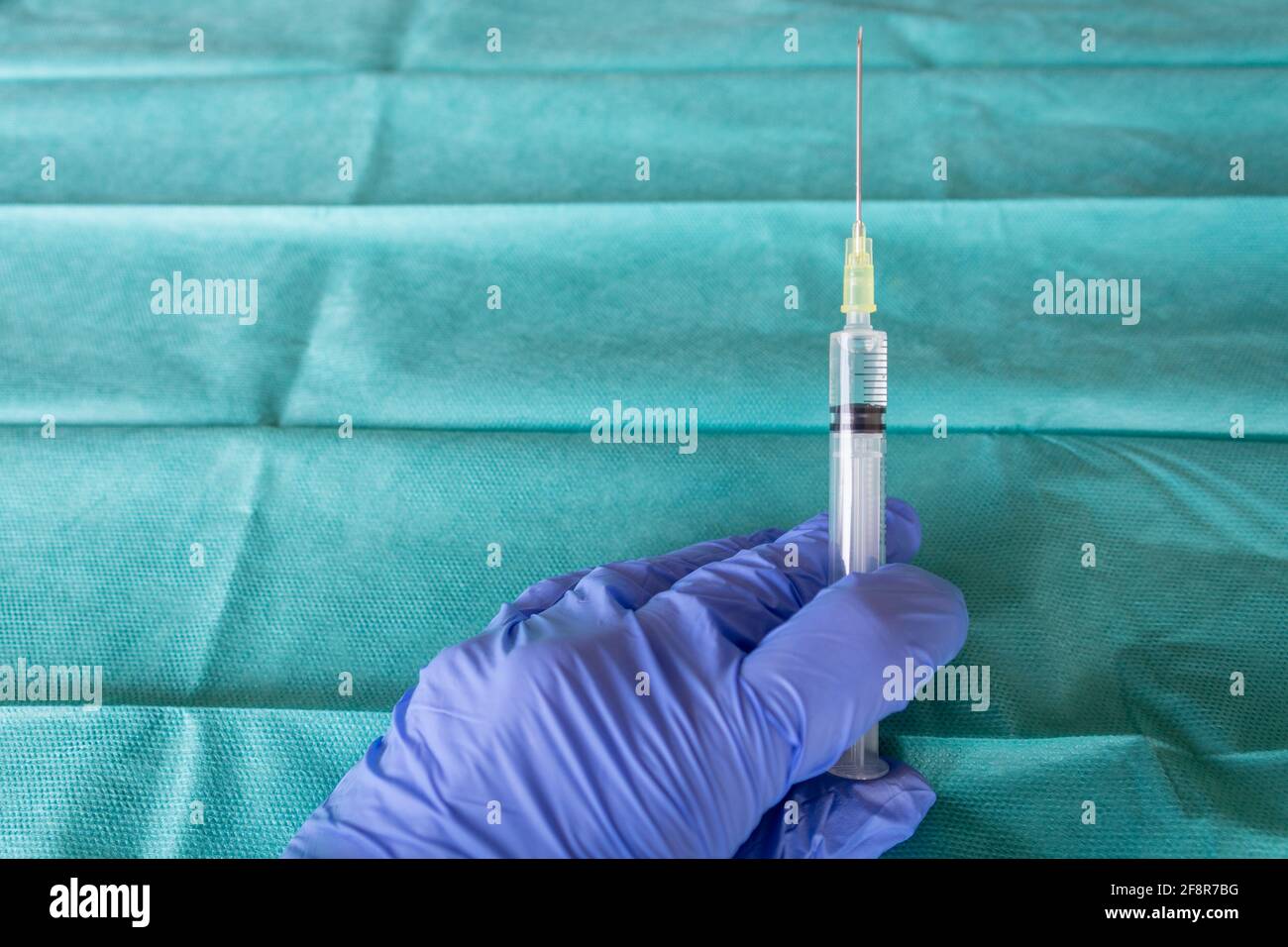 Travailleur de la santé avec des gants chirurgicaux bleus tenant une seringue devant un tissu chirurgical vert. Chirurgien main avec un vaccin. Une seringue avec le va Banque D'Images